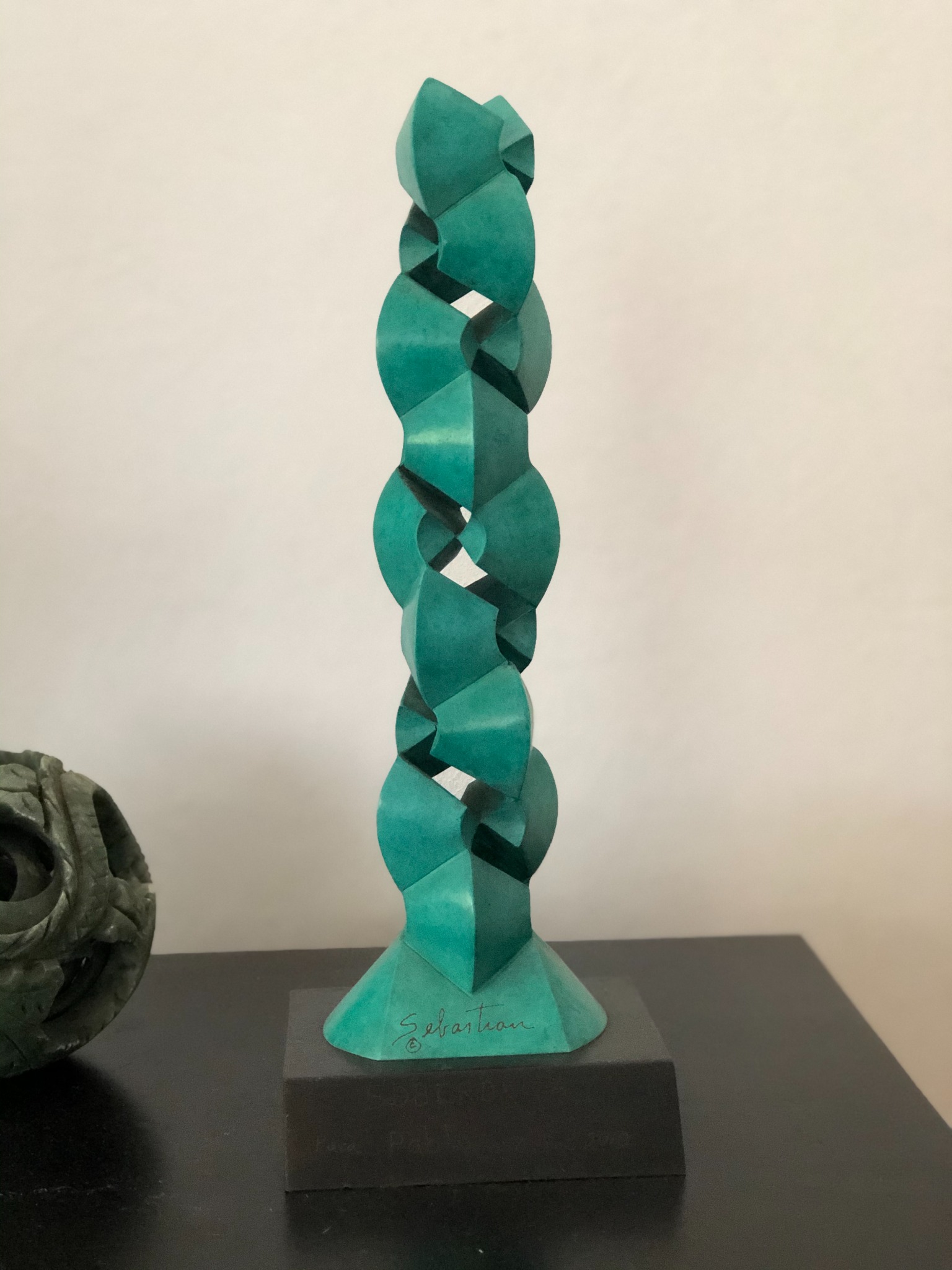 A turquoise, twisting sculpture on a dark rectangular base.